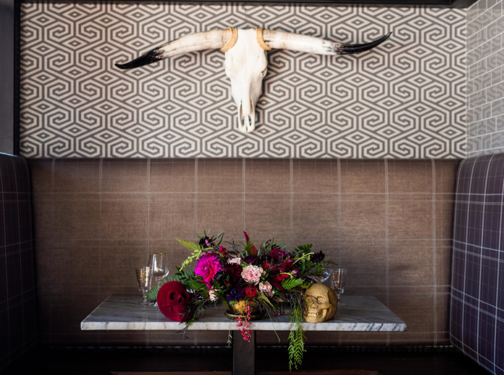 Bullhorns on a wall above a gorgeous bouquet of flowers with skull decor.