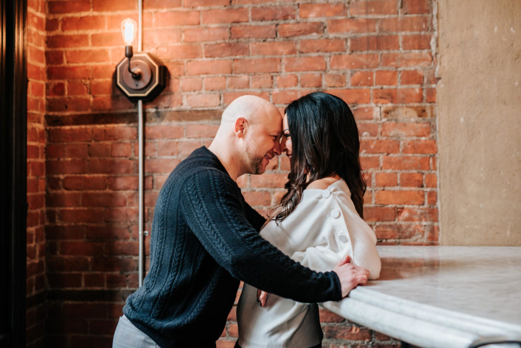 man and woman leaning against a bar top, foreheads together.