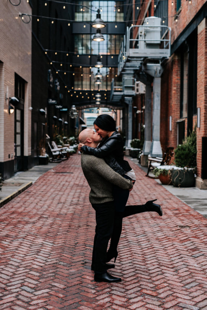 Man holding woman up kissing her in alley.