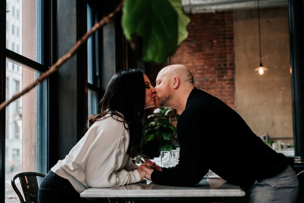 Man and woman kissing at table in a restaurant.
