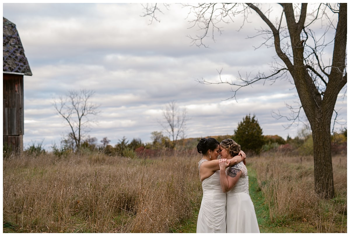 Two Brides embracing on cold fall day on backyard trail.