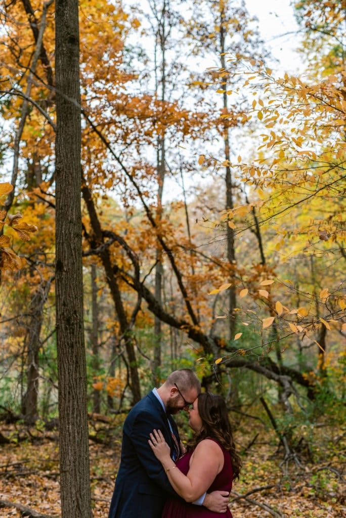 Standing in the woods, the couple is forehead to forehead pausing for an intimate moment.