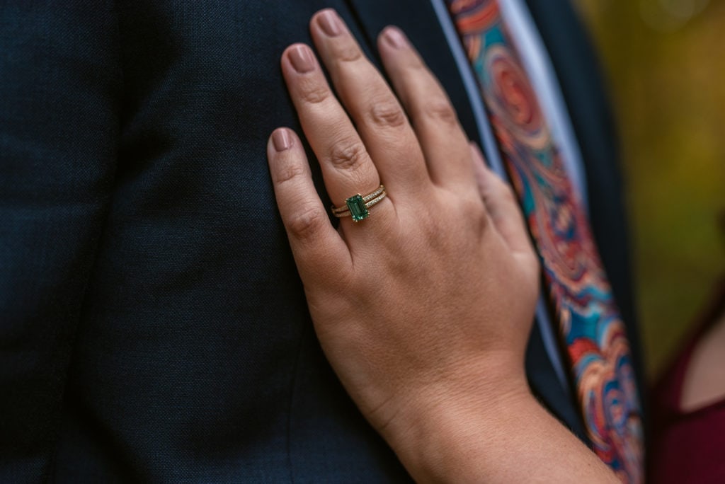 Emerald wedding ring on Bride to be's hand, while on Groom's chest.
