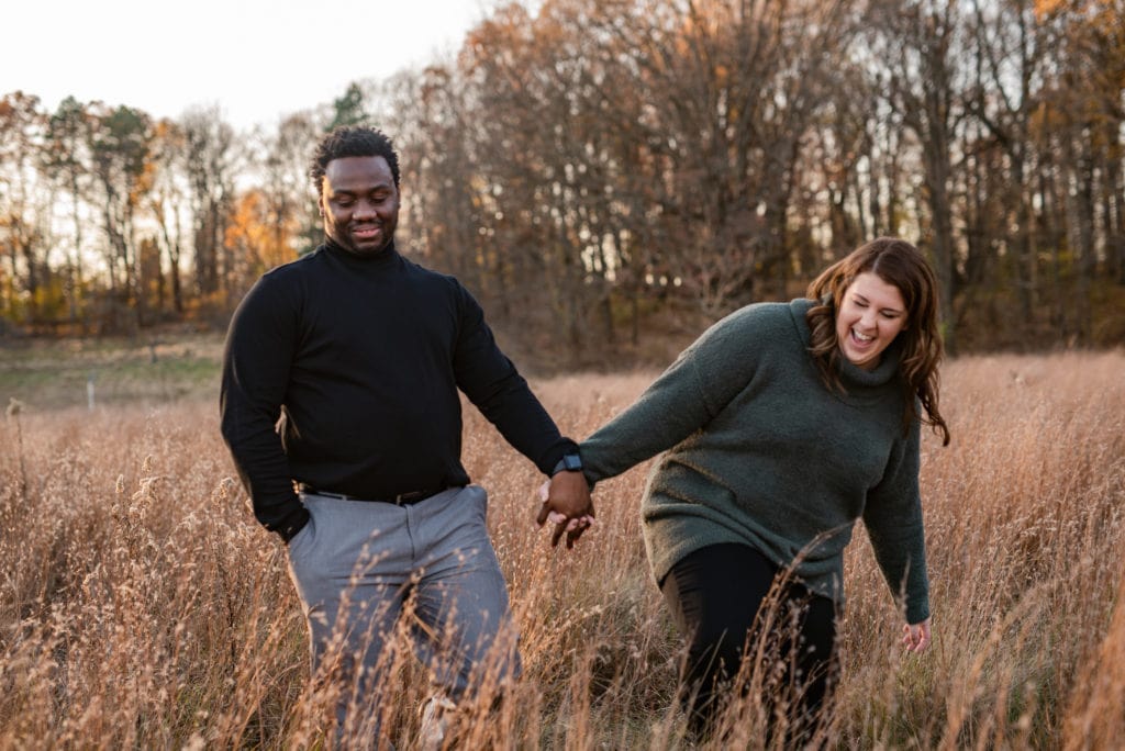 Newly engaged couple walking through tall grasses in the fall.