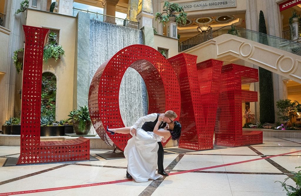 a Bride and Groom do a dip kiss in front of a large LOVE sign in the Venetian, in Las Vegas.