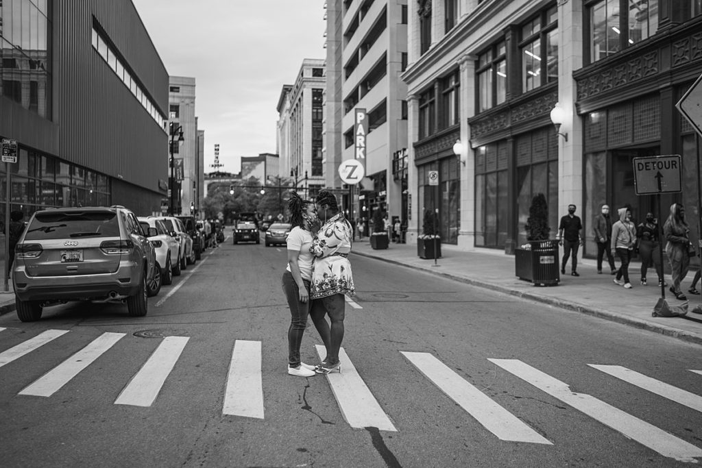 Couple standing in the streets of Detroit, kissing around a crowd of people.